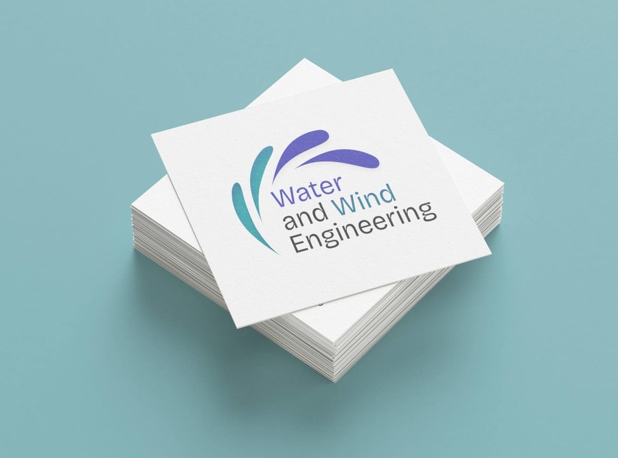Une pile de cartes de visites au format carré sur un fond bleu canard. Seule la première est visible, tournée d'un quart de tour au-dessus des autres et comporte un logo Water and Wind Engineering avec des gouttes formant un éventail au-dessus de l'écriture.